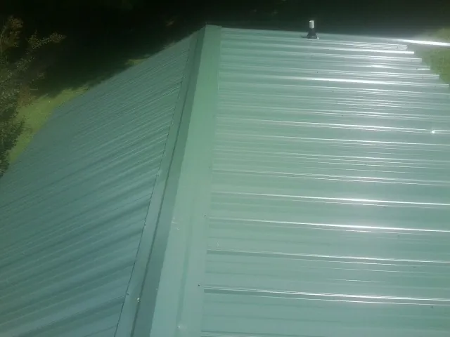 New green metal panels meeting at the ridge of a roof — Flat Roof Repair work by our crew in Yale